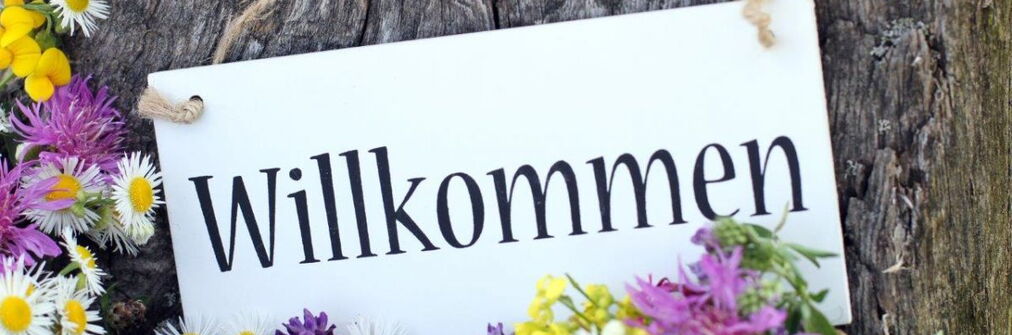 Schild mit Schrift "Willkommen" und Blumen