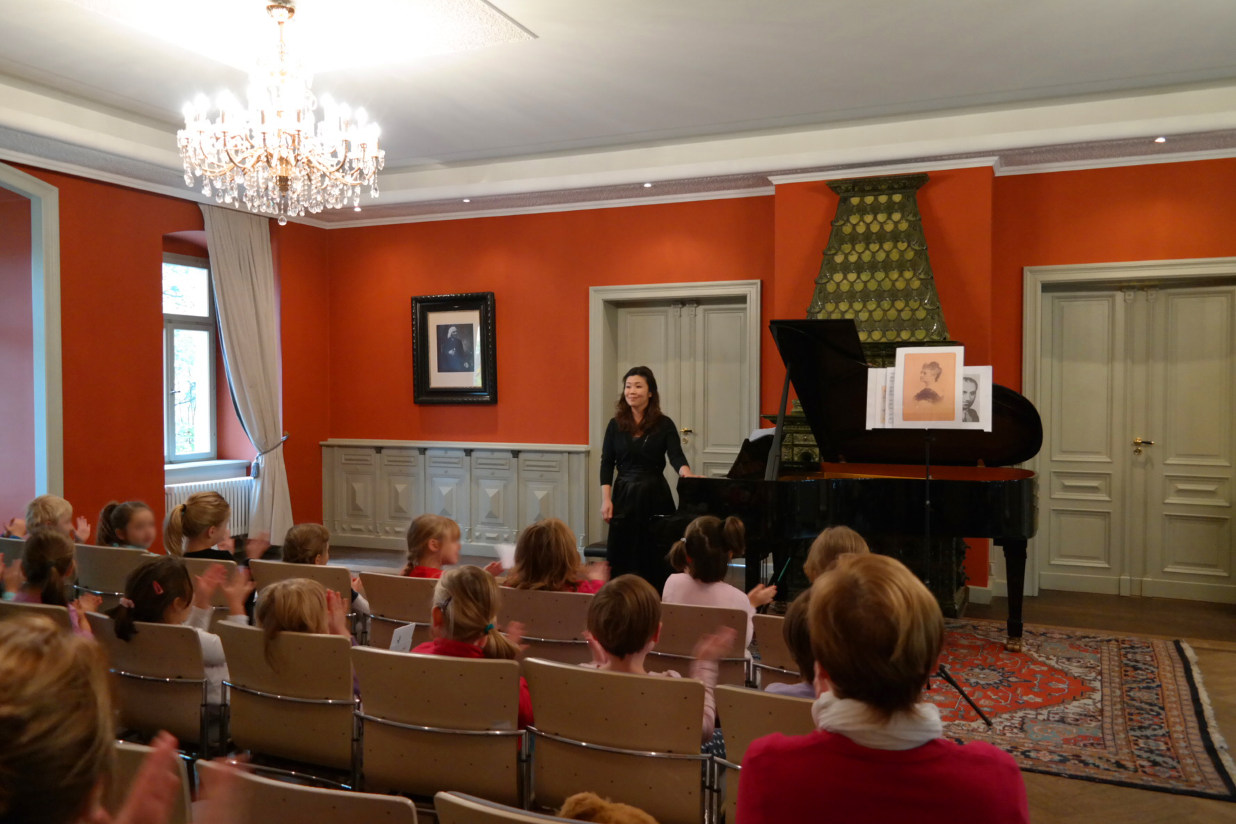Kinder sitzen in Stuhlreihen und klatschen, Pianistin steht am Flügel