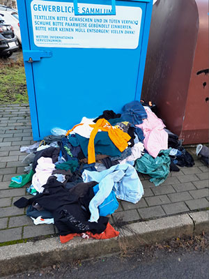 Kleidungsstücke liegen vor dem Altkleidercontainer