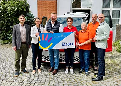 mehrerer Personen stehen mit einem Plakat vor einem Auto