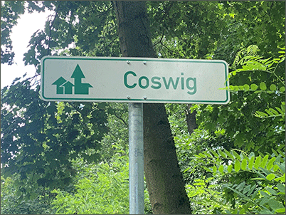weißes Verkehrsschild für Radfahrer mit grüner Schrift und Coswig als Schriftzug