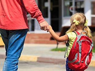 Symbolfoto Kinderbetreuung - Kind mit Rucksack an der Hand eines Erwachsenen