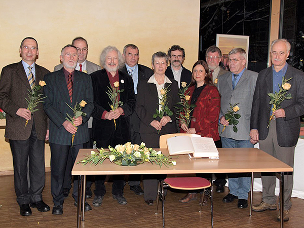 Mitglieder des "Runden Tisches" stehen hinter einem Tisch mit aufgeschlagenem Ehrenbuch und Blumenschmuck