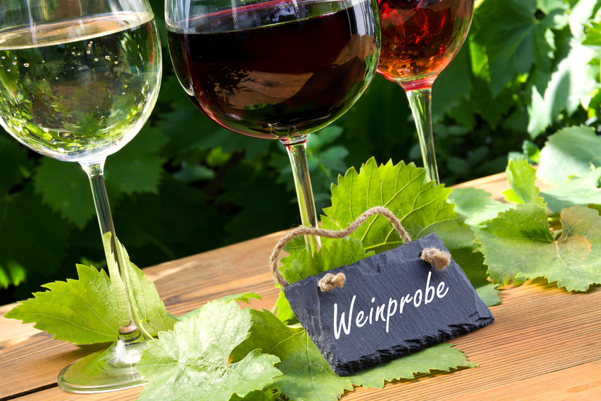 Drei Weingläser zur Weinprobe stehen auf einem Tisch mit Weinlaub dekoriert